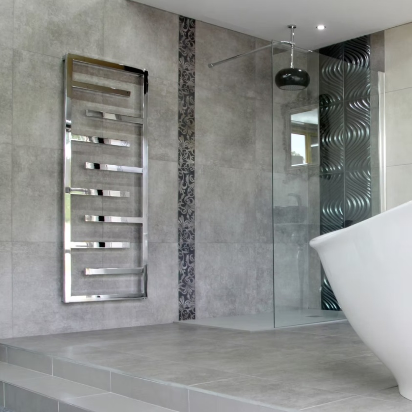 Lifestyle image of the Radox Aztec 1615mm x 600mm Chrome Designer Heated Towel Rail mounted on grey bathroom wall, next to a walk-in shower enclosure